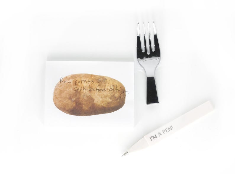 May include: A white sticky note with a brown potato illustration and the text "Raw potato - cook before eating". A white pen with the text "I'm a pen!" and a silver fork are also pictured.