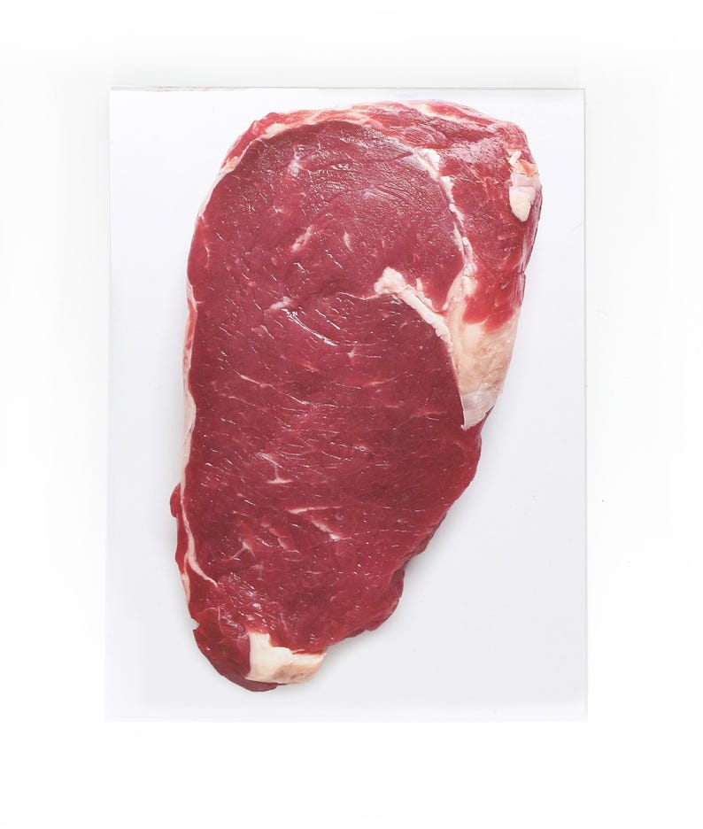May include: A raw, red beef steak with visible marbling. The steak is on a white surface.
