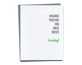 Può includere: Un biglietto bianco con il testo "HEARD YOU'RE ON BED REST. Lucky!" scritto in nero. La parola "Lucky!" è scritta in verde.