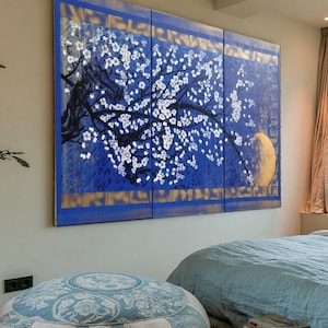a serene bedroom with a large window overlooking the ocean, a blue and white patterned ottoman, a large painting on the wall, and a stack of books on the floor.