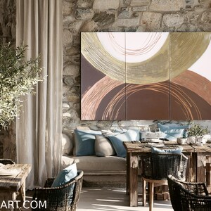 a cozy dining area with a rustic stone wall, featuring a large abstract painting as the focal point. The room is furnished with wooden tables and chairs, and the space is adorned with potted plants and other decorative elements. The overall atmosphere of the room is warm and inviting, with a harmonious blend of natural and artistic elements.