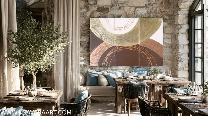 a cozy dining area with a rustic stone wall, featuring a large abstract painting as the focal point. The room is furnished with wooden tables and chairs, and the space is adorned with potted plants and other decorative elements. The overall atmosphere of the room is warm and inviting, with a harmonious blend of natural and artistic elements.