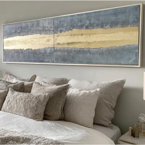 a large, long painting hanging on a wall above a bed with white bedding and multiple pillows.