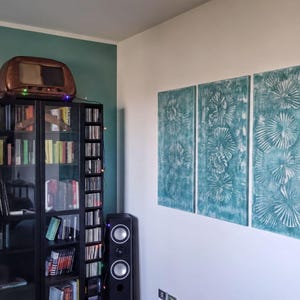 a cozy living room with a bookshelf filled with books, a television, and a speaker. The walls are painted a light blue color, and there are three large paintings hanging on the wall.