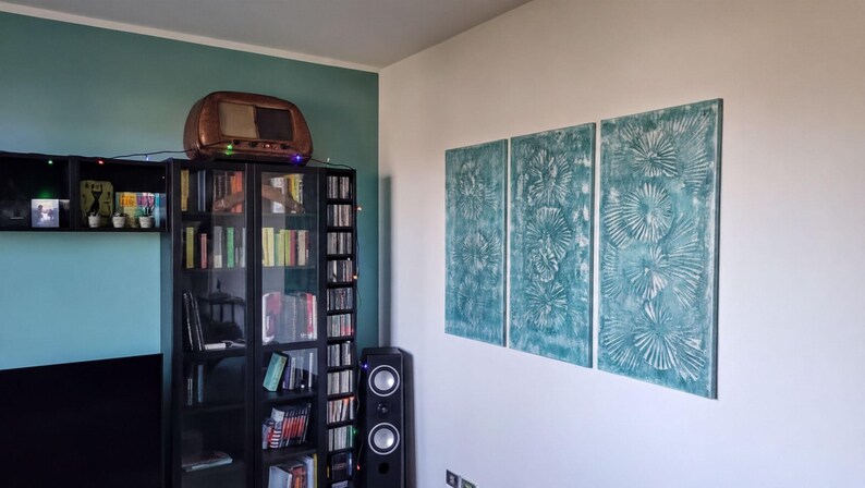 a cozy living room with a bookshelf filled with books, a television, and a speaker. The walls are painted a light blue color, and there are three large paintings hanging on the wall.