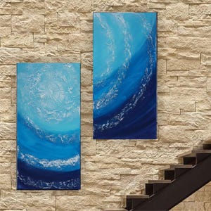 two large paintings hanging on a stone wall, depicting a blue and white abstract design.