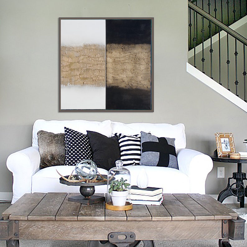 Peut inclure: Tableau abstrait encadr&eacute;, divis&eacute; en trois sections verticales : blanc, texture dor&eacute;e et noir. Un canap&eacute; blanc avec des coussins d&eacute;coratifs et une table basse en bois sont devant l'&oelig;uvre d'art.