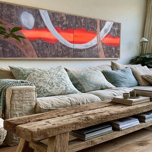 a cozy living room with a large window, a comfortable sofa with pillows, a wooden coffee table, and a large abstract painting on the wall.