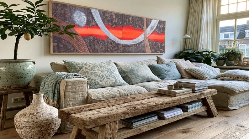 a cozy living room with a large window, a comfortable sofa with pillows, a wooden coffee table, and a large abstract painting on the wall.