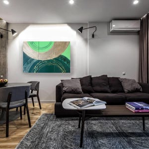 a modern living room with a black sofa, a wooden coffee table, and a dining table with chairs. The room has a minimalist and contemporary design, with a large abstract painting on the wall and a window with curtains.