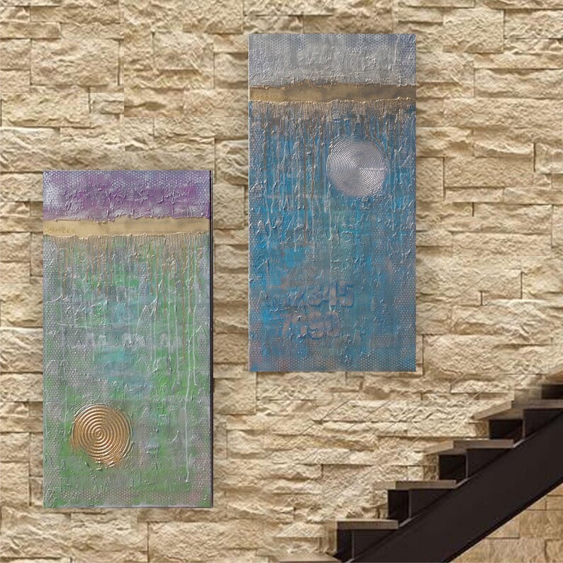 two abstract paintings hanging on a brick wall, with a staircase visible in the background.