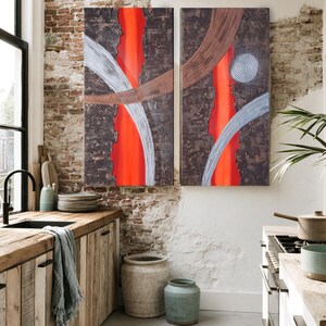 a modern kitchen with a large abstract painting hanging on the wall above a wooden counter. The kitchen features a rustic wooden counter, a sink, and various kitchen accessories such as bowls, cups, and a potted plant. The overall design has a mix of natural and industrial elements, creating a visually appealing and functional space.