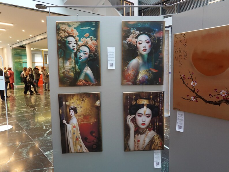 May include: Four framed paintings on display at an art exhibition. The paintings feature women in traditional Asian clothing and imagery. One painting depicts a woman with a crown and jewelry, another shows two women with flowers in their hair, and a third features a woman with a flower in her hair and a fish behind her. The fourth painting is a landscape with a branch of cherry blossoms and a large orange circle.