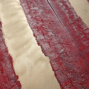 a close-up view of a textured surface with a red and white striped pattern. The surface appears to be a combination of red and white paint or material, with a metallic or metallic-like texture. The image does not contain any discernible objects or actions, and there are no specific actions or movements depicted. The focus is on the texture and pattern of the surface.
