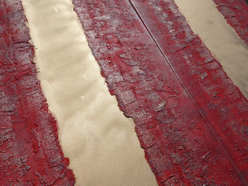 a close-up view of a textured surface with a red and white striped pattern. The surface appears to be a combination of red and white paint or material, with a metallic or metallic-like texture. The image does not contain any discernible objects or actions, and there are no specific actions or movements depicted. The focus is on the texture and pattern of the surface.