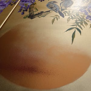 a close-up view of a painting with a large circular shape in the center, surrounded by various elements such as birds, leaves, and flowers. The painting appears to be a close-up of a larger artwork, possibly a collage or a section of a larger painting.