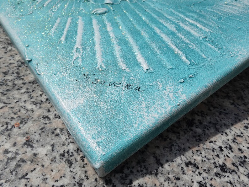 a close-up view of a textured surface, possibly a piece of artwork or a decorative object, with a turquoise or blue-green hue. The surface appears to be made of a material with a textured or embossed appearance, and there is a signature or text written on it.