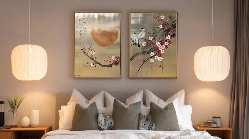 a serene bedroom scene with a large bed adorned with white pillows and a gray comforter. Above the bed, two framed paintings hang on the wall, one depicting a cherry blossom tree with pink flowers and the other showing a bird perched on a branch. The room is illuminated by two pendant lights hanging from the ceiling, creating a warm and inviting atmosphere.