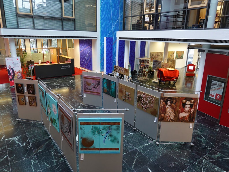 Puede incluir: Una galer&iacute;a de arte exhibe una colecci&oacute;n de pinturas enmarcadas de inspiraci&oacute;n asi&aacute;tica. Las obras presentan temas florales y de geishas, con una variedad de colores y estilos. La galer&iacute;a est&aacute; ubicada en un edificio moderno con suelo de m&aacute;rmol.