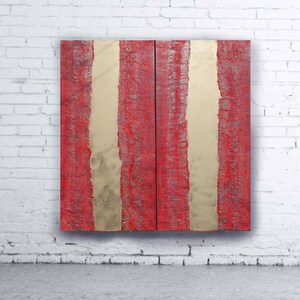 a striking red and gold abstract artwork displayed on a white brick wall.