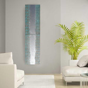 a modern living room with a tall, vertical abstract painting hanging on the wall. The room is furnished with two white sofas and a large potted plant, creating a serene and contemporary atmosphere.