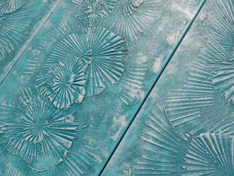 a close-up view of a textured surface with a pattern of overlapping, circular shapes painted in a turquoise color. The surface appears to be made of wood or a similar material, with a rough, textured finish.