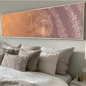 a large, rectangular artwork hanging on a wall above a bed with white bedding and pillows.