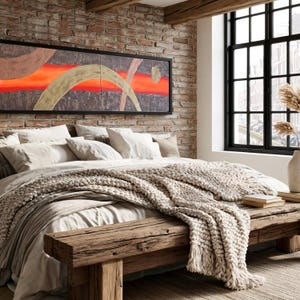 a cozy bedroom with a large bed, a wooden bench, and a brick wall with a framed abstract painting above it. The room has a rustic and modern aesthetic, with a large window providing natural light and a view of the city outside.