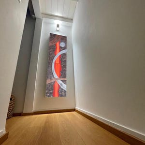 a hallway with a wooden floor and white walls. There is a large abstract painting hanging on the wall, which appears to be the focal point of the hallway.