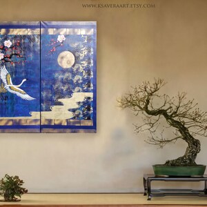 a serene indoor setting with a large blue and gold painting of a crane in flight above a bonsai tree on a wooden stand. The painting is framed by a blue border and is hung on a wall above a small table with a plant on it.