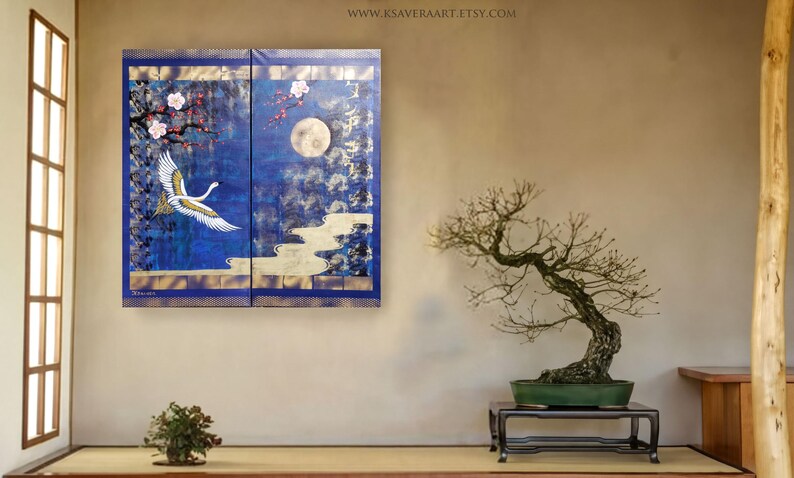 a serene indoor setting with a large blue and gold painting of a crane in flight above a bonsai tree on a wooden stand. The painting is framed by a blue border and is hung on a wall above a small table with a plant on it.