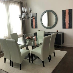 a modern dining room with a glass-topped dining table surrounded by white chairs. The room has a minimalist and elegant design, with a large mirror on the wall and a chandelier hanging above the table.