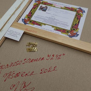 a Japanese calligraphy piece with a certificate of authenticity, a wooden frame, and some gold hardware.
