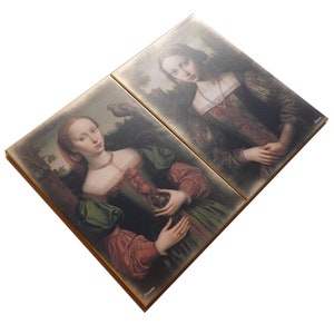 May include: Two framed paintings of women in Renaissance-style clothing. The woman on the left is holding a small object in her hand. The woman on the right is standing with her hands clasped in front of her.