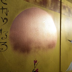 The image is a close-up of a painting featuring a large, round shape resembling a sun or moon, with a bird in flight in the background.
