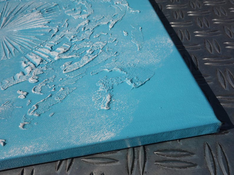 a close-up view of a blue canvas with a textured surface, possibly created using a technique like sanding or scratching. The canvas is placed on a metal surface, which has a diamond pattern.