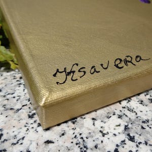 a close-up view of a gold-colored surface, possibly a piece of paper or a book, with the word "SAVVERA" written in black ink on it.