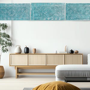 a modern living room with a wooden cabinet, a white sofa, and a yellow throw pillow. The room has a minimalist and clean design, with a white wall and a large abstract painting above the cabinet.