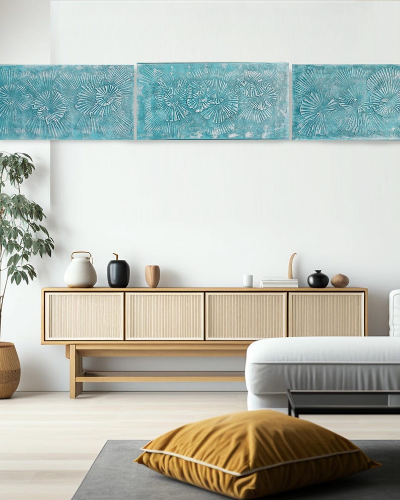 a modern living room with a wooden cabinet, a white sofa, and a yellow throw pillow. The room has a minimalist and clean design, with a white wall and a large abstract painting above the cabinet.