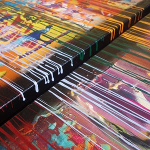 The image is a close-up of a vibrant, abstract painting with bold colors and dynamic brushstrokes. The painting features a mix of red, yellow, green, and blue hues, creating a visually striking and energetic composition.