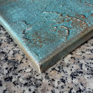 a close-up view of a textured surface, possibly a piece of art or a canvas, with a metallic or textured finish. The surface appears to be a combination of different materials, such as metal and stone, creating a visually interesting and textured appearance.
