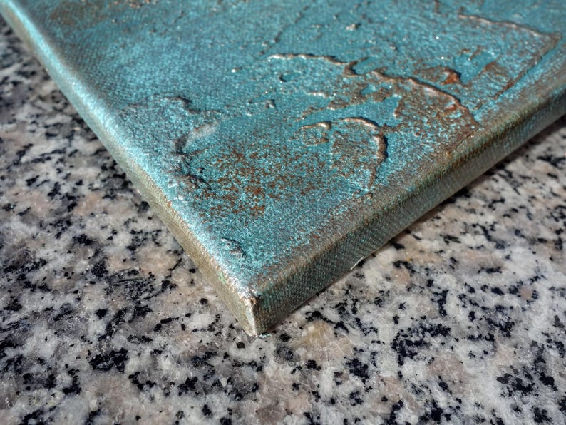 a close-up view of a textured surface, possibly a piece of art or a canvas, with a metallic or textured finish. The surface appears to be a combination of different materials, such as metal and stone, creating a visually interesting and textured appearance.