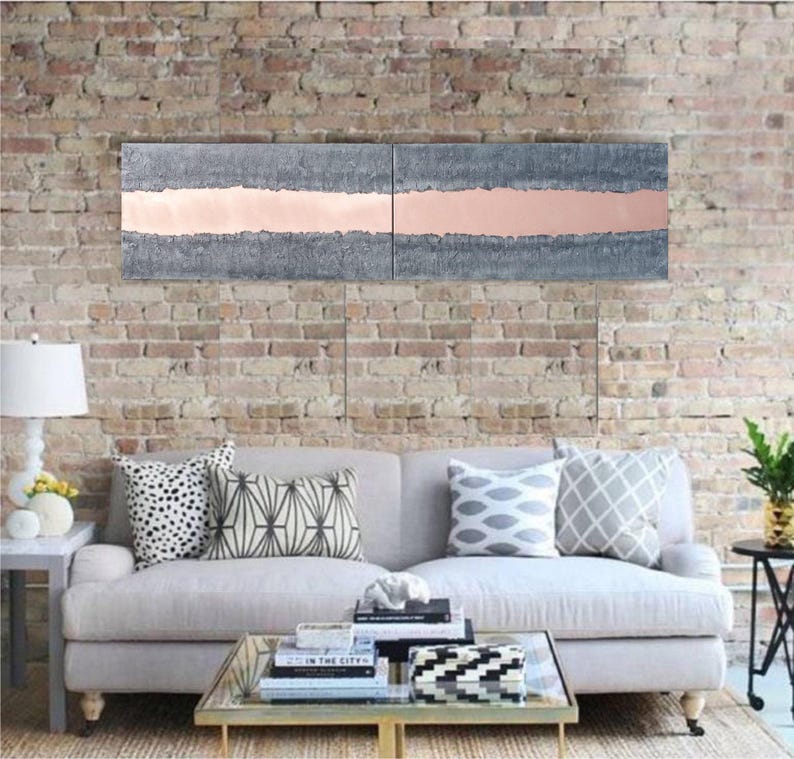 a modern living room with a gray sofa adorned with patterned throw pillows, a glass coffee table, and a brick wall backdrop. Above the sofa, there is a large abstract painting with a horizontal stripe in shades of gray and pink.