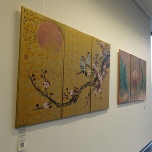 two large paintings hanging on a wall, depicting a branch with flowers and birds.