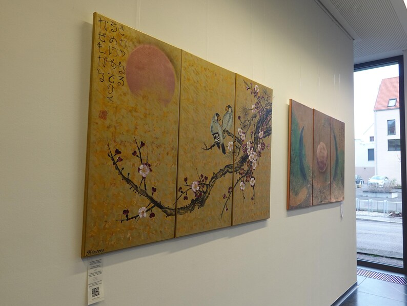 two large paintings hanging on a wall, depicting a branch with flowers and birds.