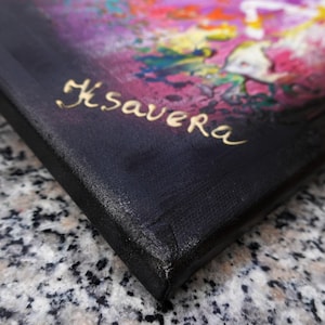 The image is a close-up of a black canvas with a colorful painting on it. The name "K.SAVERA" is written in gold cursive on the canvas.