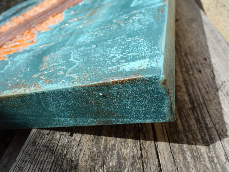 a close-up view of a weathered, blue-green surface with a rust-colored element, possibly a metal or metal-like material, attached to it. The surface appears to be a wooden board or piece of wood, with a rough, textured appearance.