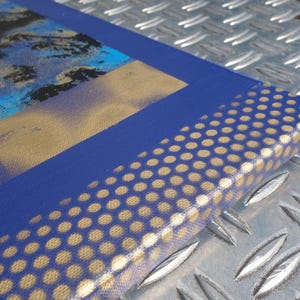 a close-up view of a blue and gold patterned surface, possibly a canvas or a piece of fabric, with a metallic texture.
