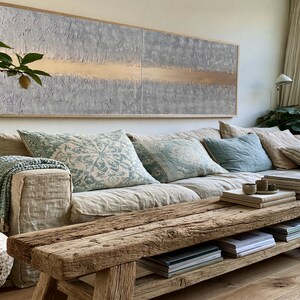 a cozy living room with a large window, a comfortable sofa with patterned pillows, a wooden coffee table, and various decorative elements such as a potted plant, a vase, and a painting on the wall.