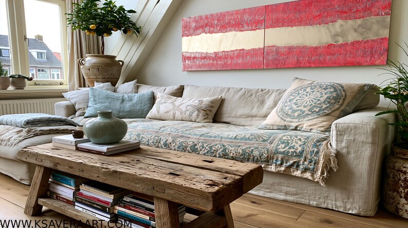 a cozy living room with a large, comfortable couch adorned with patterned pillows and a throw blanket. A wooden coffee table sits in front of the couch, and a large, colorful abstract painting hangs on the wall above it. The room is decorated with various plants and books, creating a warm and inviting atmosphere.